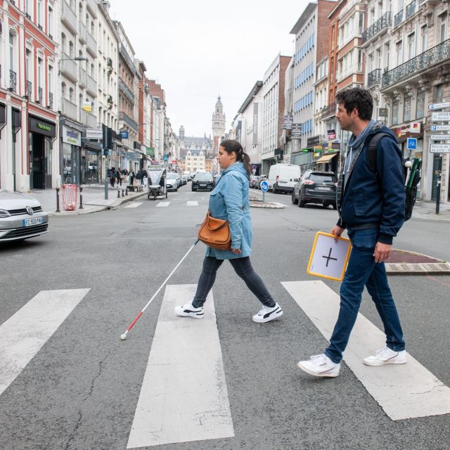 Deux personnes traversant un passage piéton dont une femme avec une canne blanche